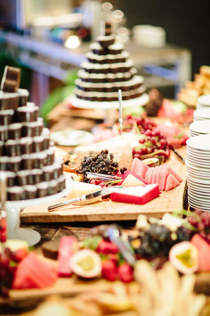 A party grazing table showing a variety of cheese, fruit and 2 cake towers of chocolate heart-shaped brownies